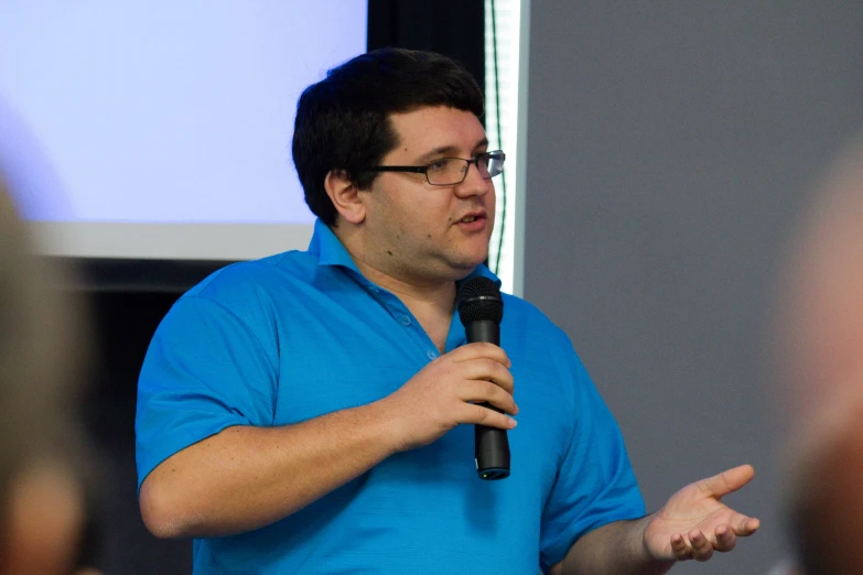 a man wearing a blue shirt holding a microphone and speaking