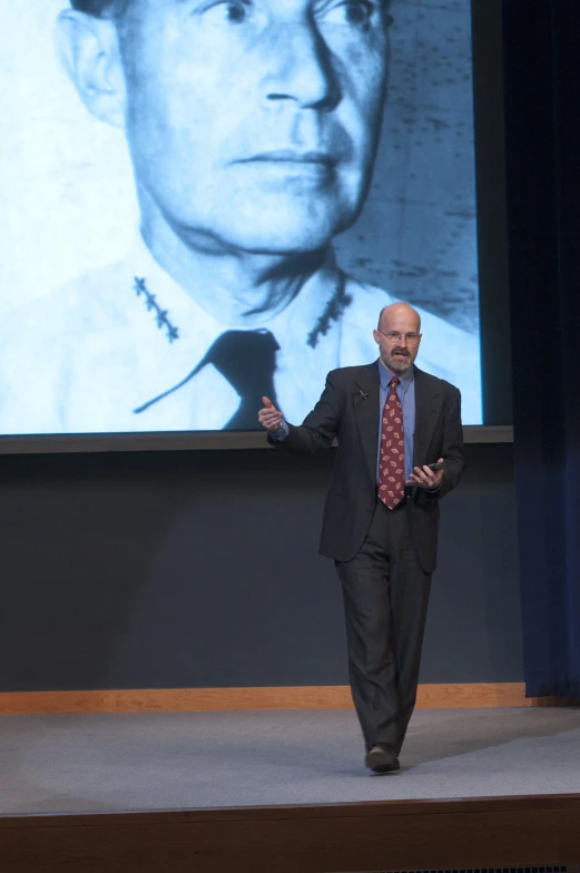 a man is walking down the runway in front of a projection of an older person