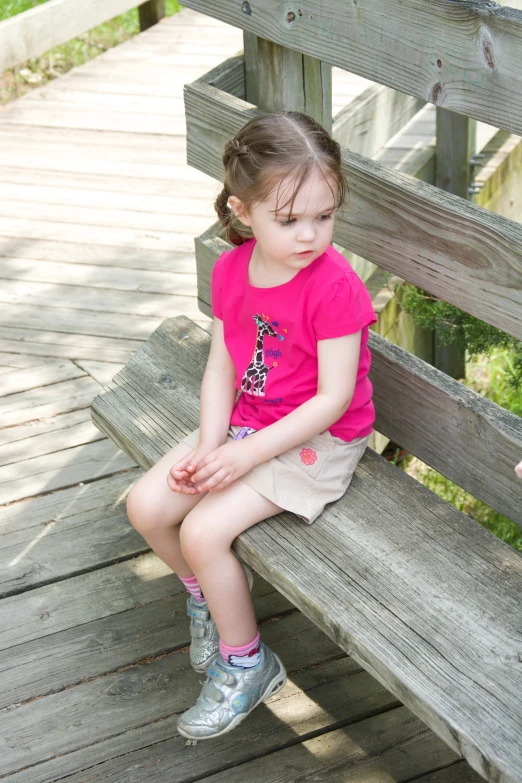 a little girl sitting on a bench looking at the ground