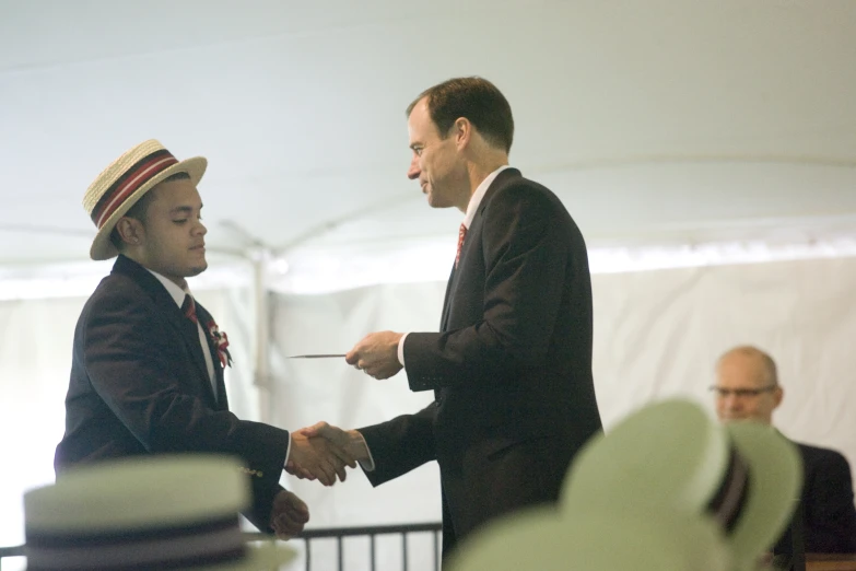 two men shaking hands and wearing hats with one woman