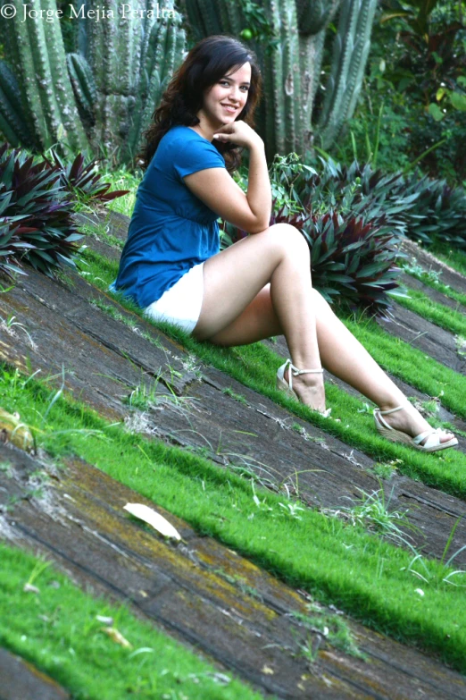 a woman sitting on a lawn with a cactus in the background