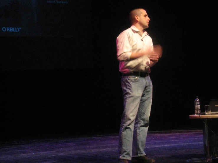 a man stands on a stage in front of the microphone, looking at the screen