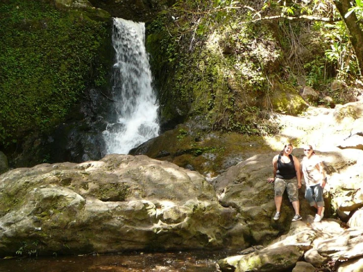 two people standing by rocks near a waterfall