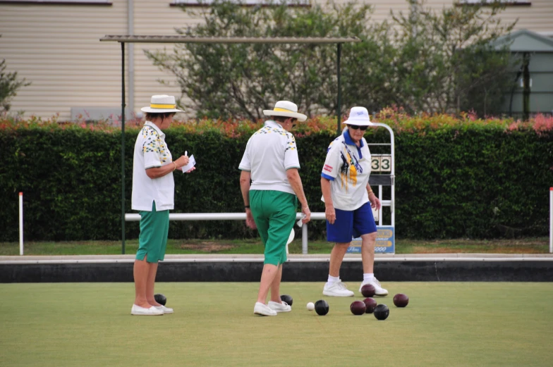 three men are playing bowls on the green