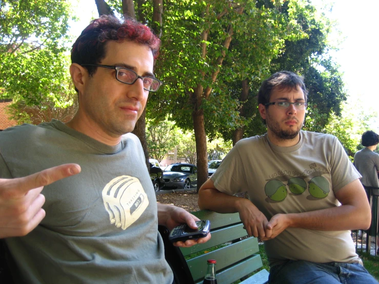 two men sitting on a park bench holding a cell phone