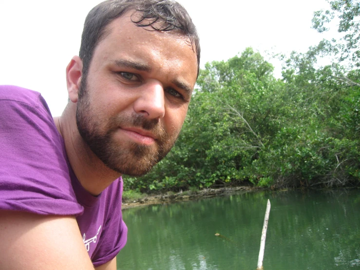 a man with a beard on standing in front of a lake