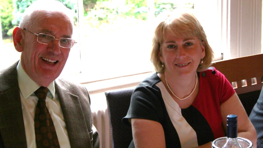 two smiling people seated at a table with wine glasses