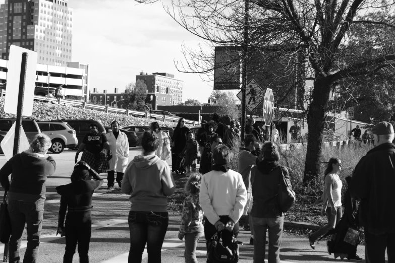 many people walk on the sidewalk, and cars in the background