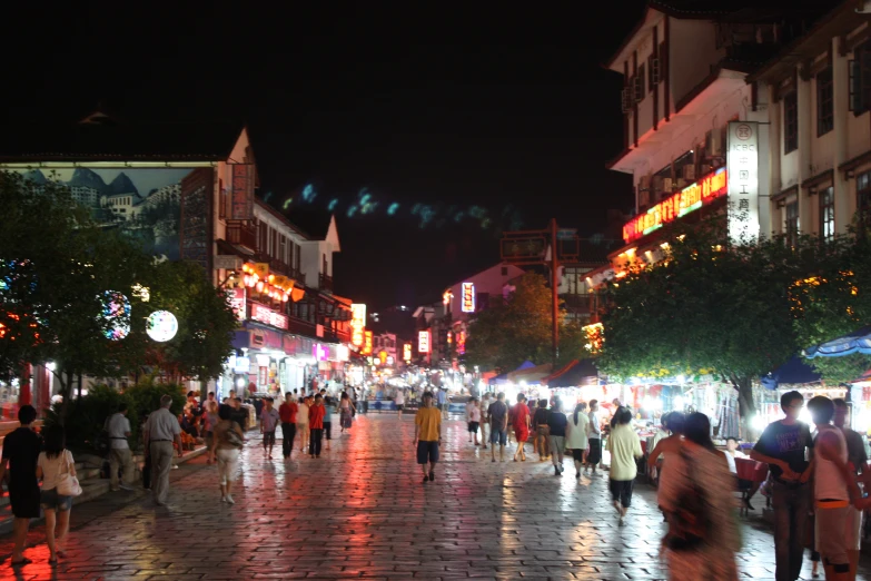 an outdoor plaza with people and shops at night