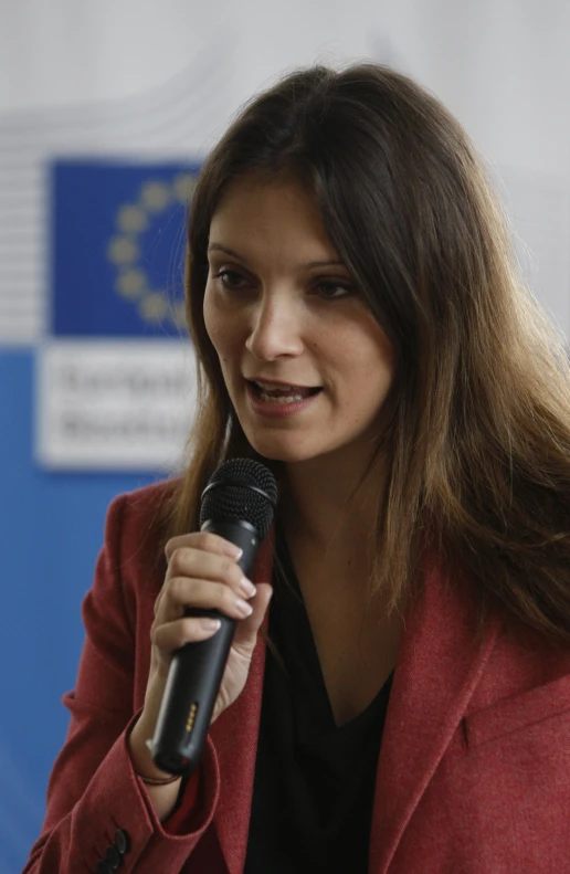 woman speaking into microphone in front of wall and flag