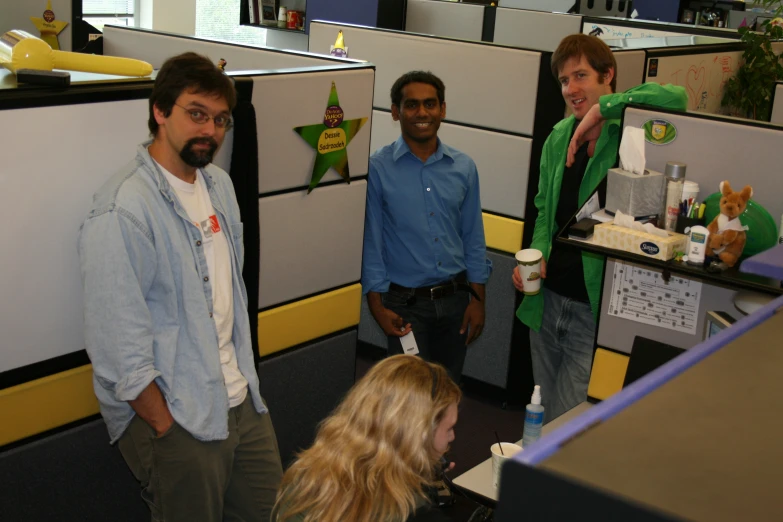 three men standing in an office cubicle talking to a lady