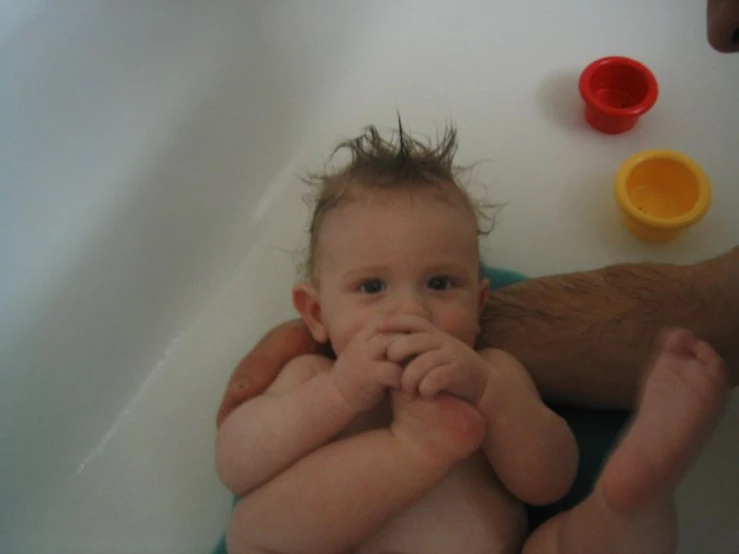 a baby sitting on his mother in the bathtub