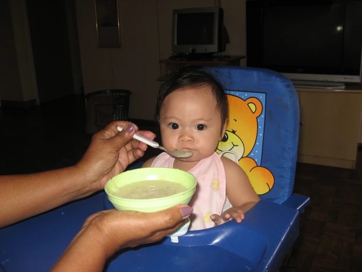 an adult feeds a baby feeding it a bowl
