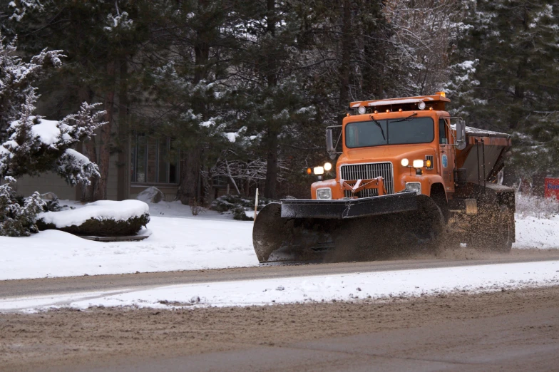 an orange truck is plowing a road during winter