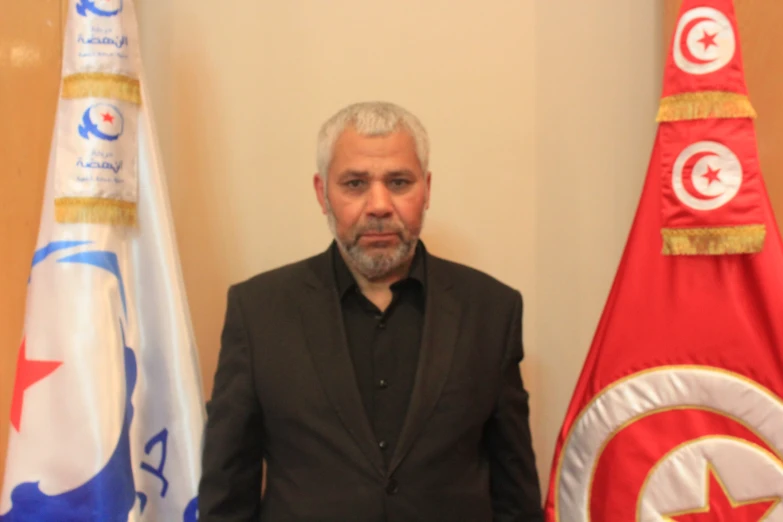 an older man stands near a row of flags