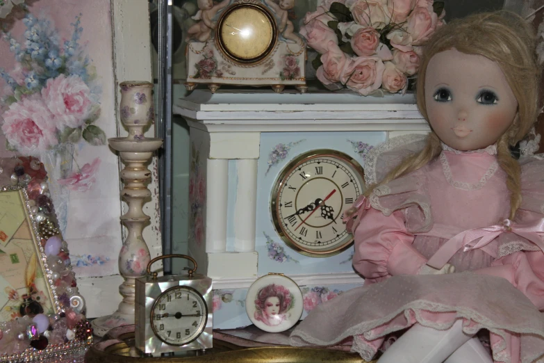 a pink doll with long hair sits on a small table next to a clock and other decorative objects