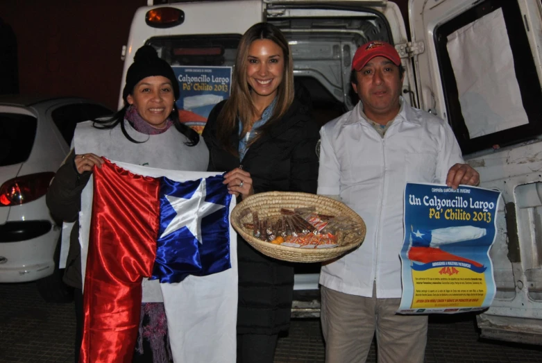 three people standing in front of a truck holding up a flag
