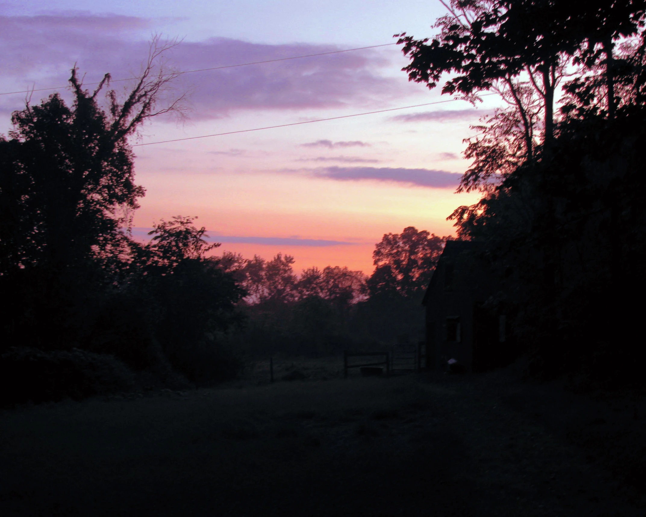 there is a house in the distance next to a tree line