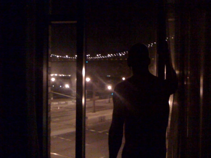 the silhouette of a man behind a curtain of a window at night