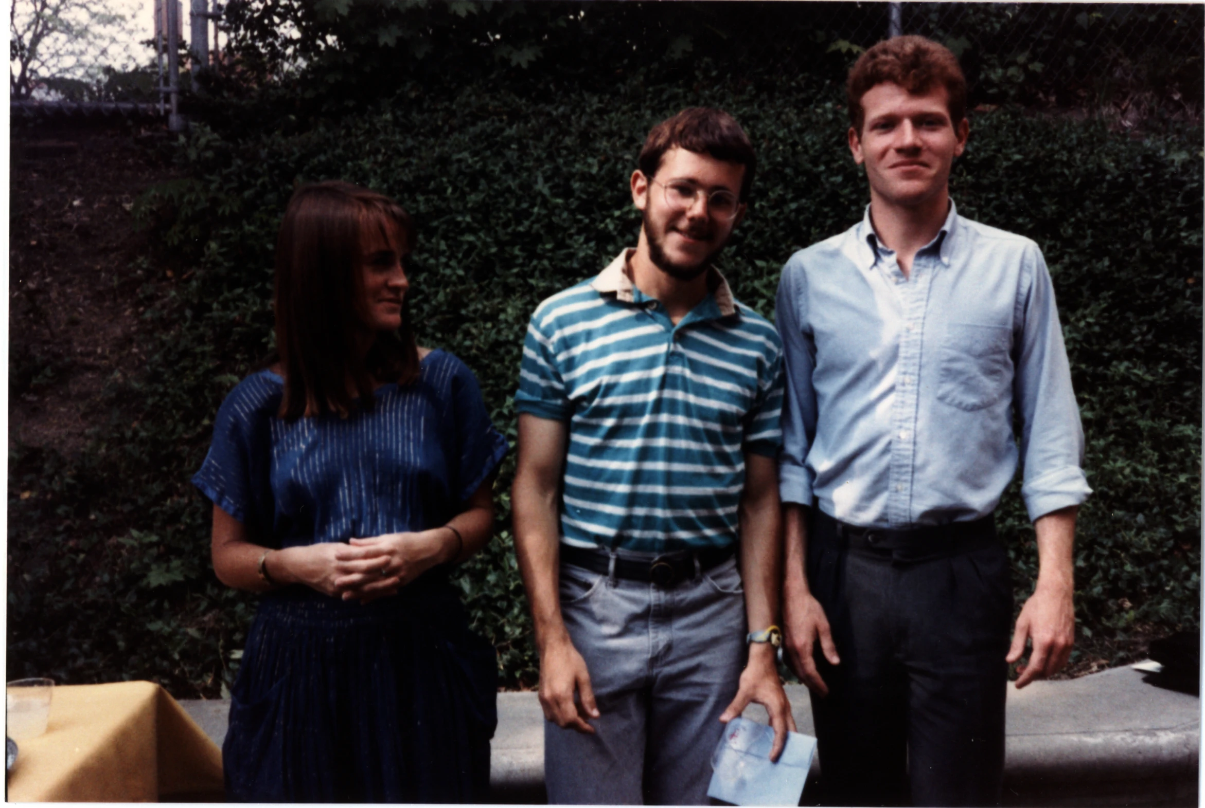 three people standing next to each other in front of a bush