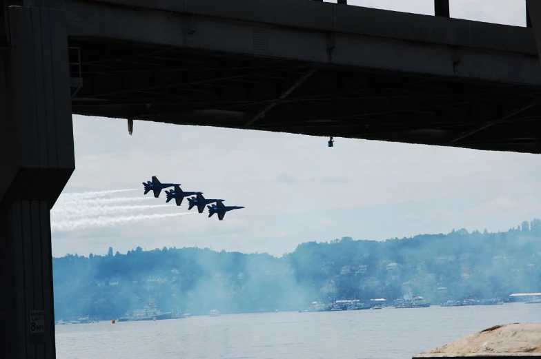 two airplanes flying over water under a bridge