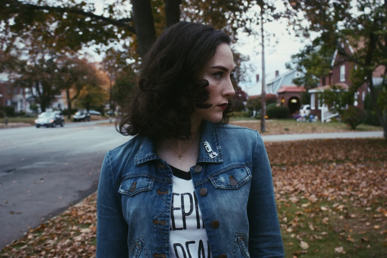 a woman in a denim jacket standing on a street with autumn leaves