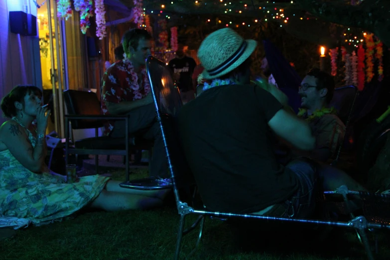 a person with a hat sitting in a chair while others stand and sit around