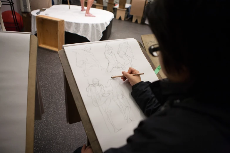 a person drawing in an art studio with others looking on