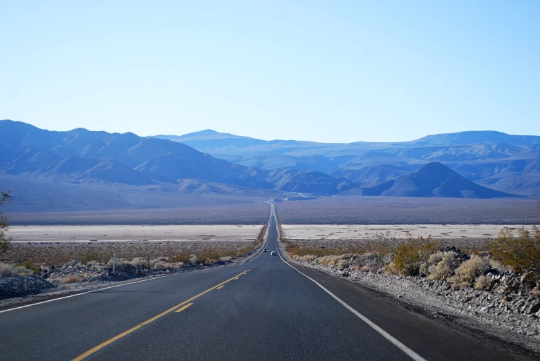 a long, empty highway leads towards mountains on either side