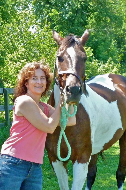 a woman standing by a brown and white horse