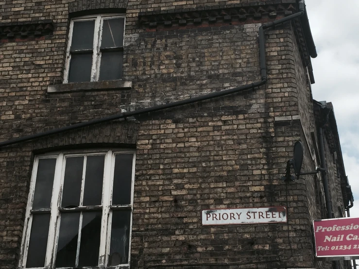 a brick building with three white windows, two red signs hanging on the outside