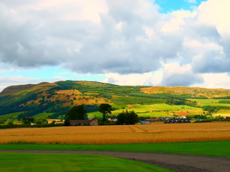 a dirt road runs past green grass and tall hills