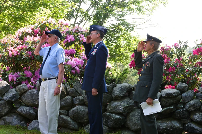 three military personnel are standing by some flowers