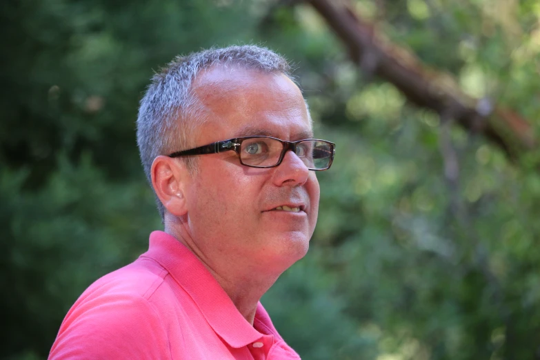 a man with glasses on in front of trees