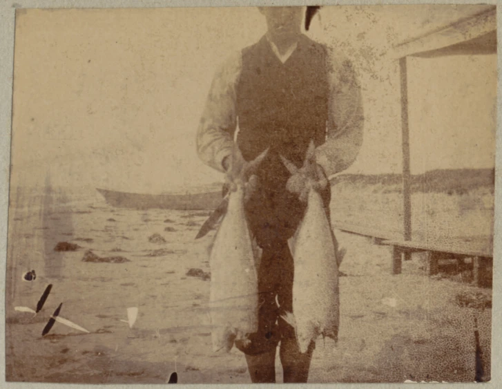 a man holding some fish standing on a beach