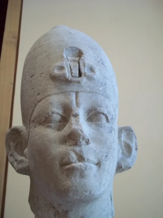 an ancient statue, depicting a person's head with a piece of art on top