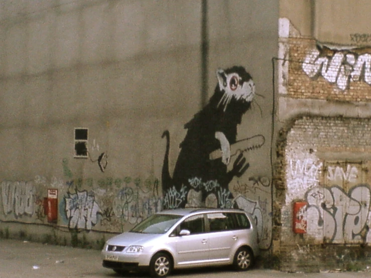 a small white car parked in front of graffiti on a wall