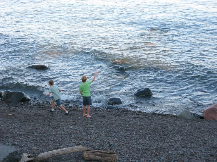 two boys standing on beach next to water holding hands up