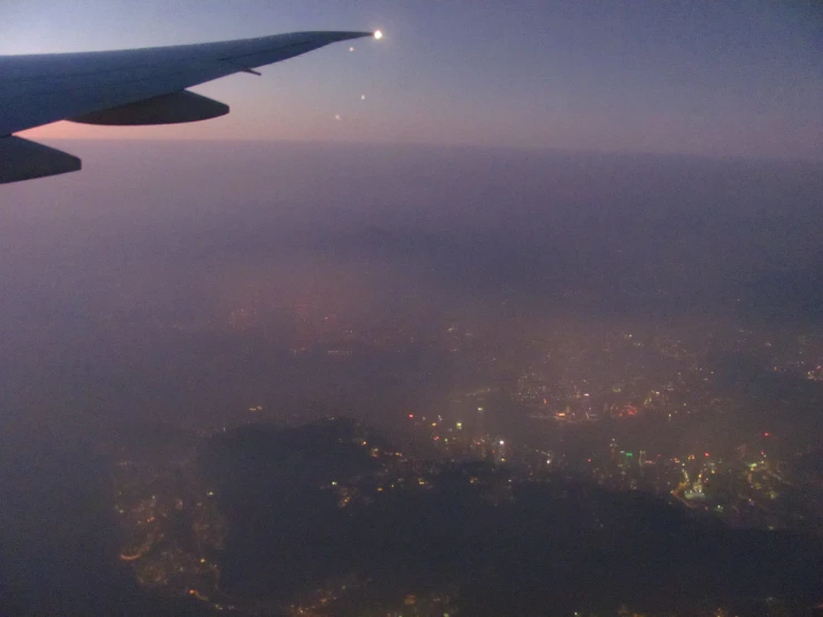 an aerial view from inside an airplane shows the wing and side of buildings in the horizon