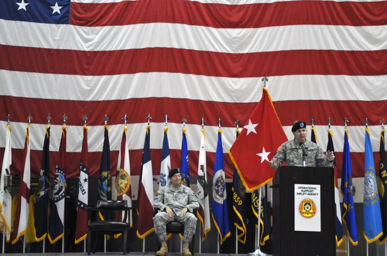 two military men speaking in front of american flags