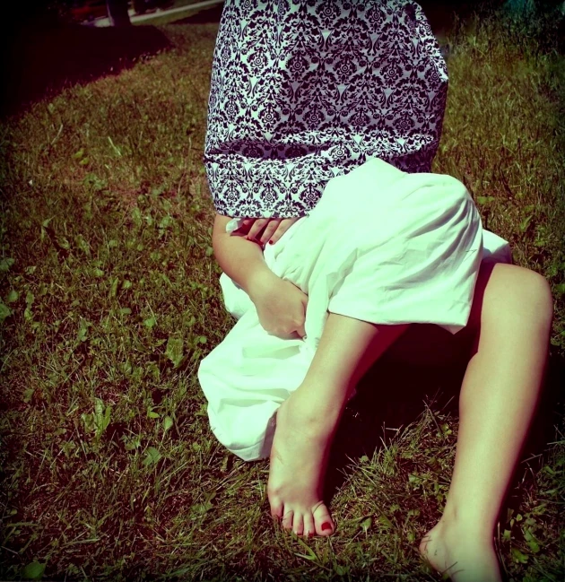 a woman sitting in the grass with her bare feet propped against her stomach