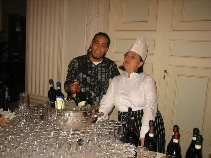 two chefs and a waitress are standing next to a table with wine glasses on it