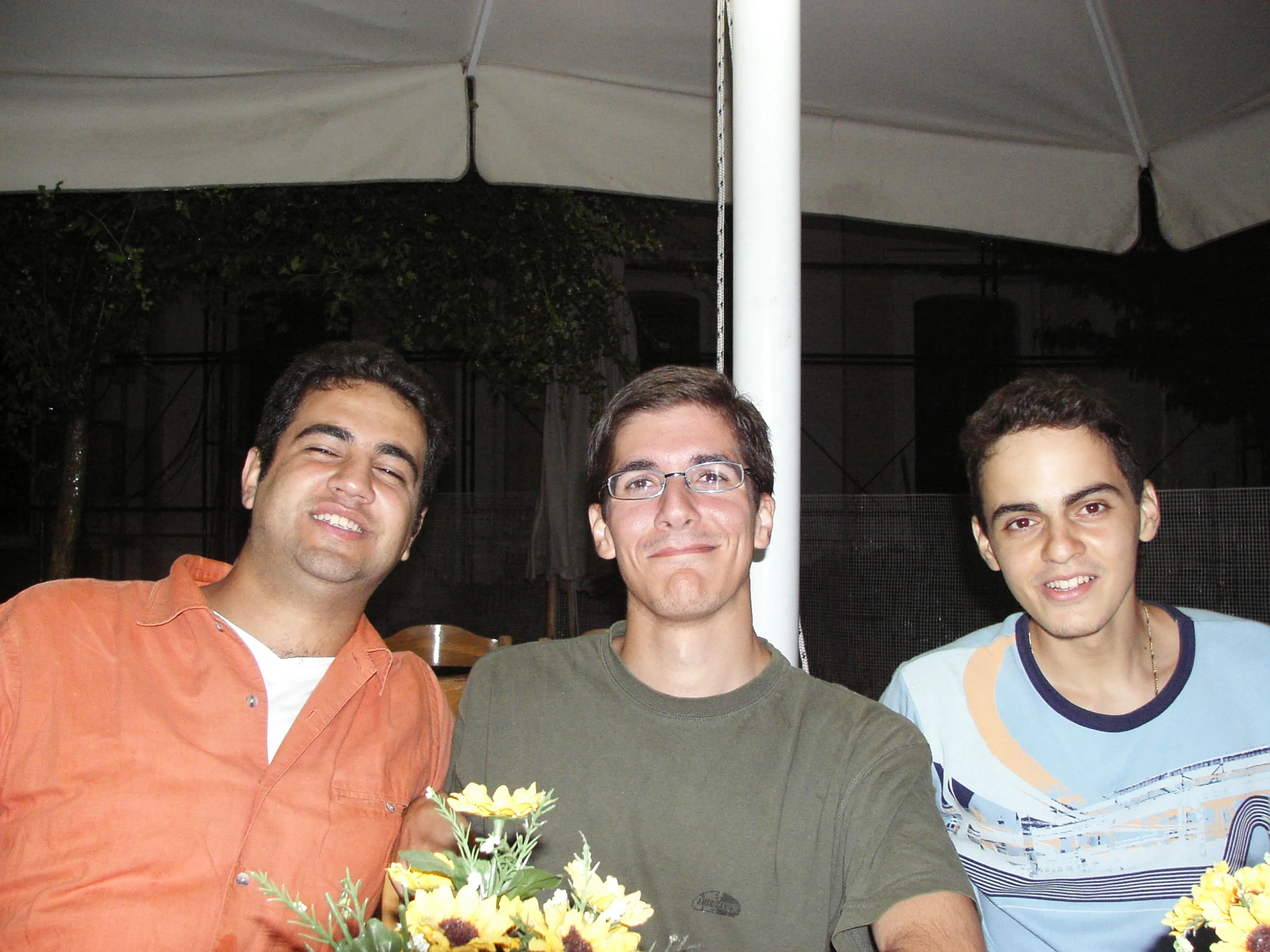 three men smile under a tent on a sunny day