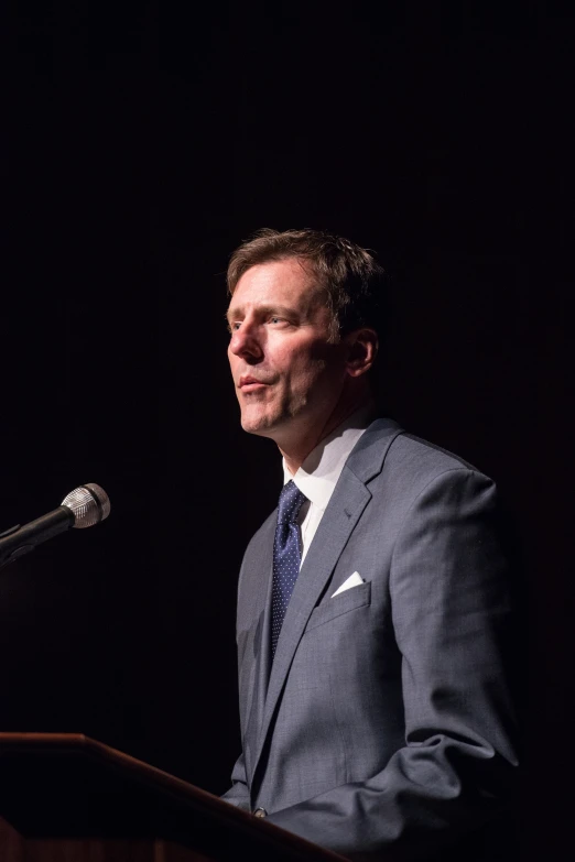 a man in a suit speaks at a podium