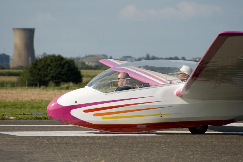 two people ride in the front of a white, pink and orange aircraft