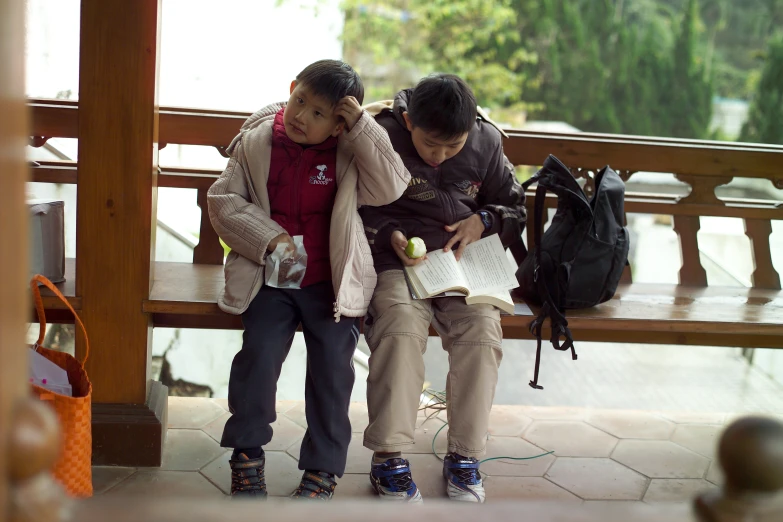 two asian people sitting on a bench reading
