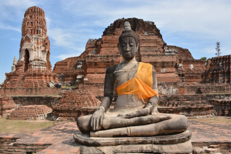 a buddha statue is posed in a park near a ruined temple