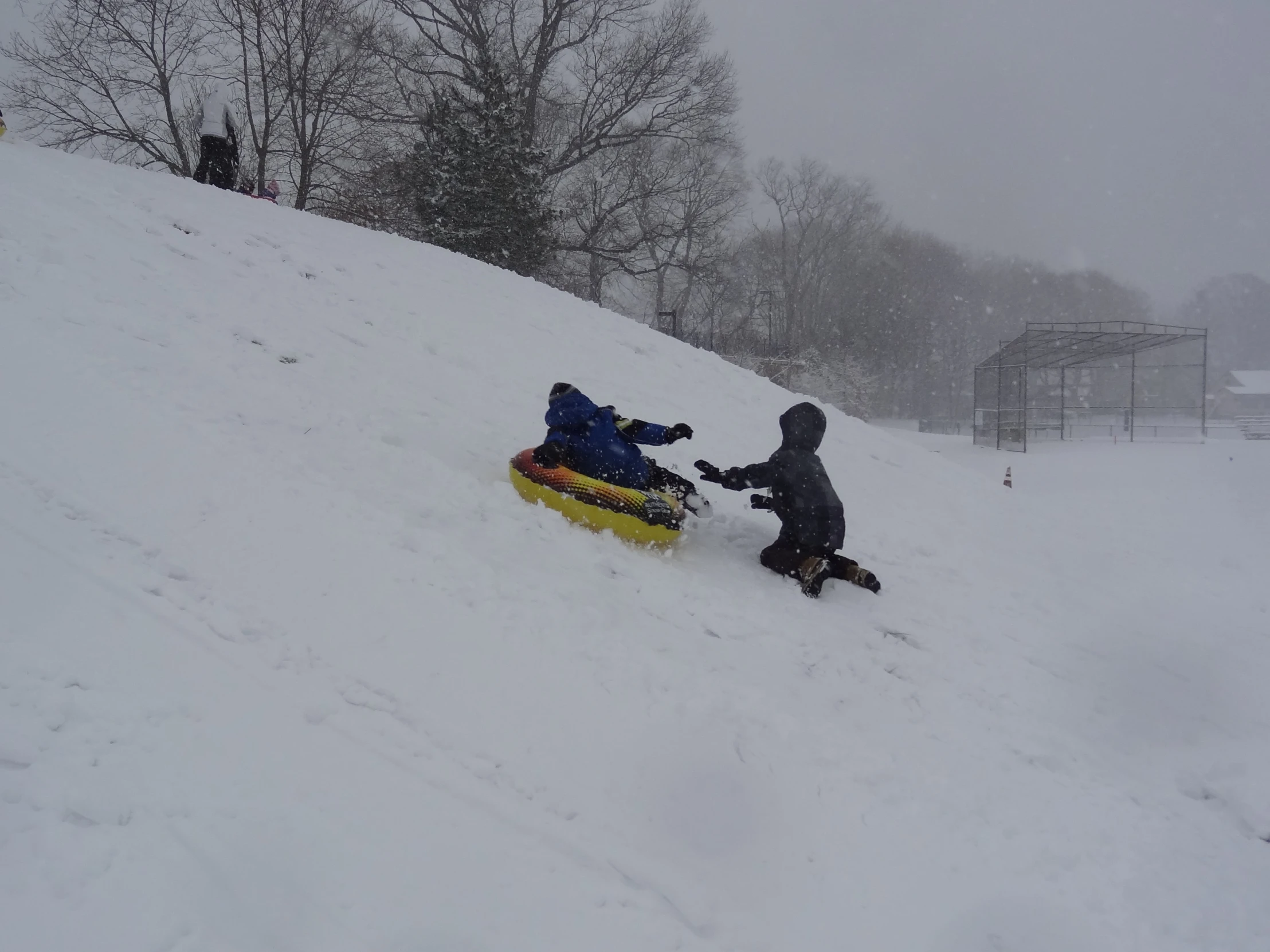 a person on a sled pulling another man across a snow bank