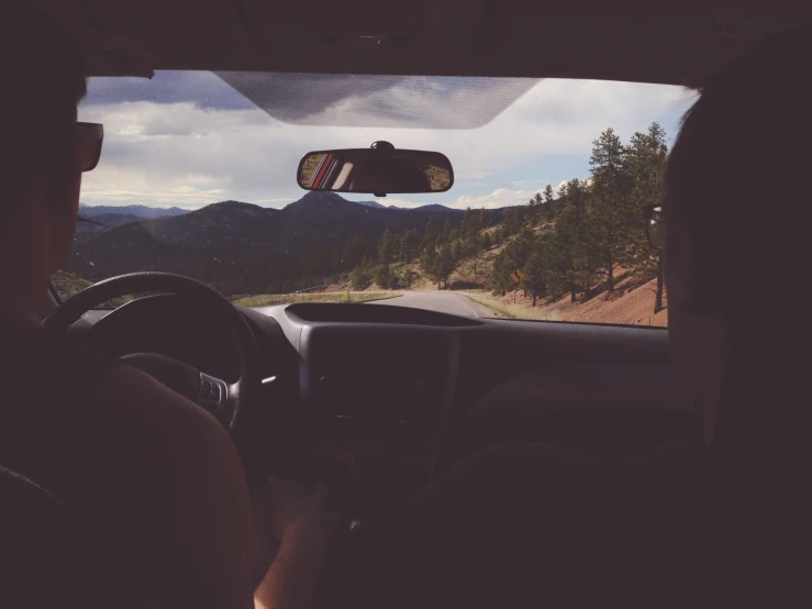 man in automobile looking out mountain road toward wooded area