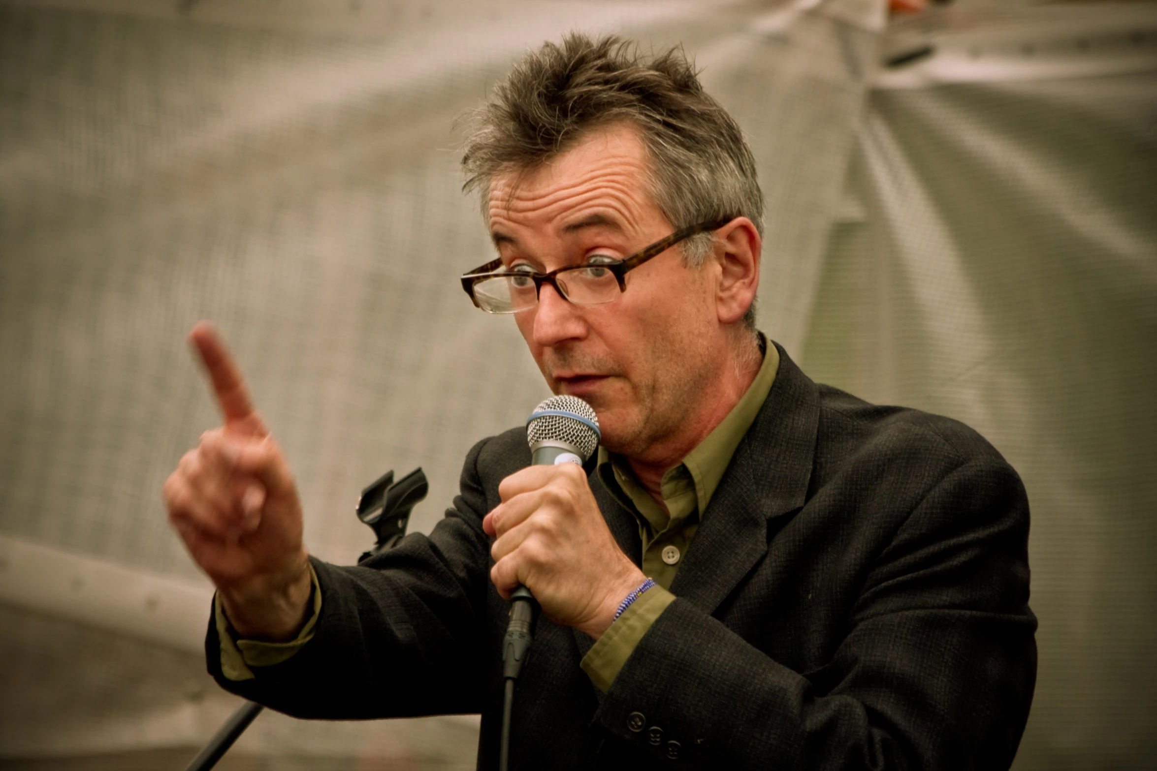 a man in glasses holds a microphone up while talking